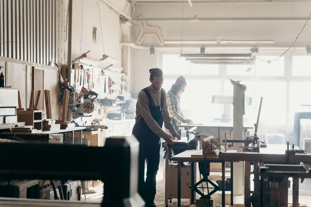 Two craftsmen working in a sunny workshop, focusing on carpentry projects.