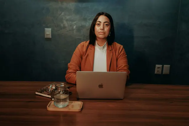 Confident woman in business attire working at a laptop in an office setting.