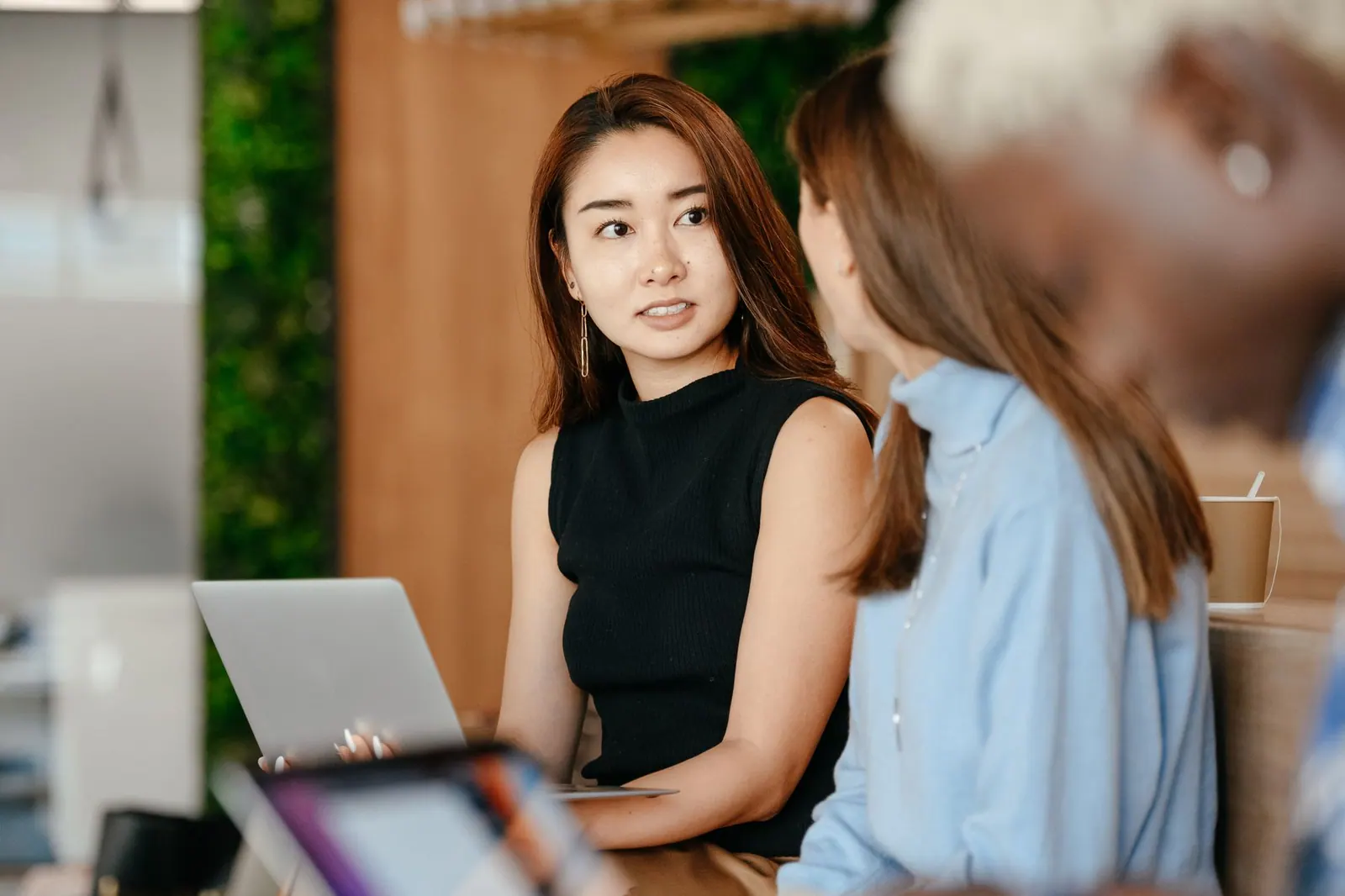 Serious ethnic female with laptop talking with anonymous business partners about job in office