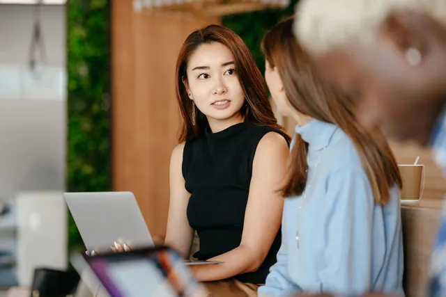 Serious ethnic female with laptop talking with anonymous business partners about job in office