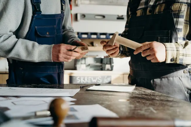 Two craftsmen working on a woodworking project in a well-lit workshop.