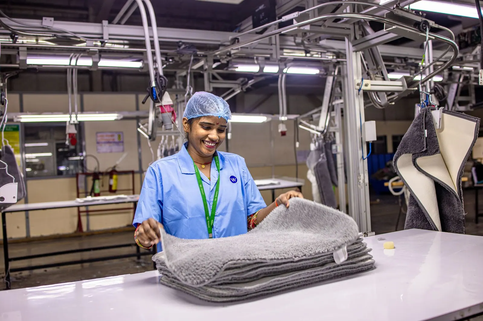 Smiling female worker folding textiles in a modern factory setting.
