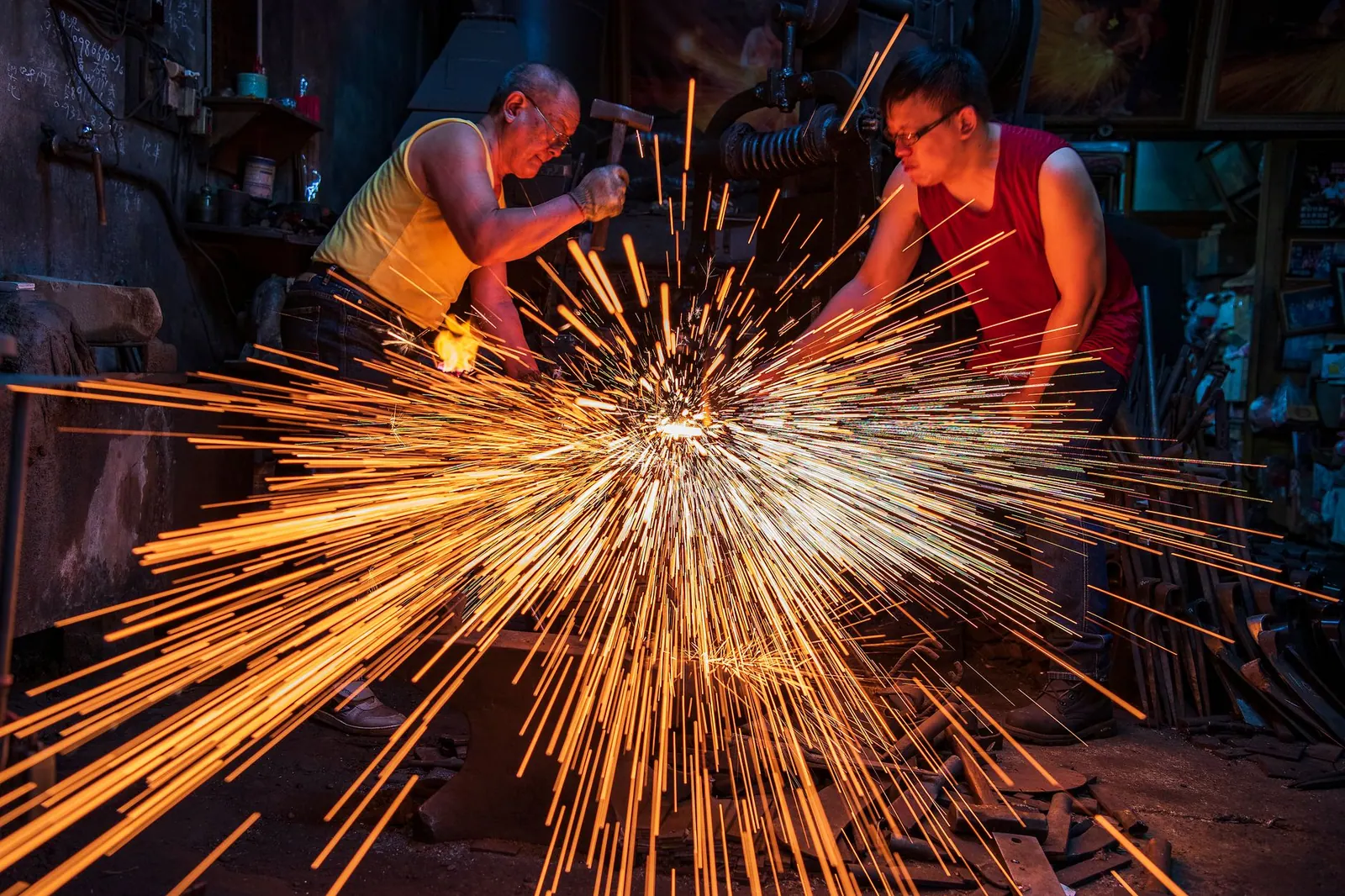 Blacksmiths in Taiwan handcraft metal with sparks flying in an industrial workshop.