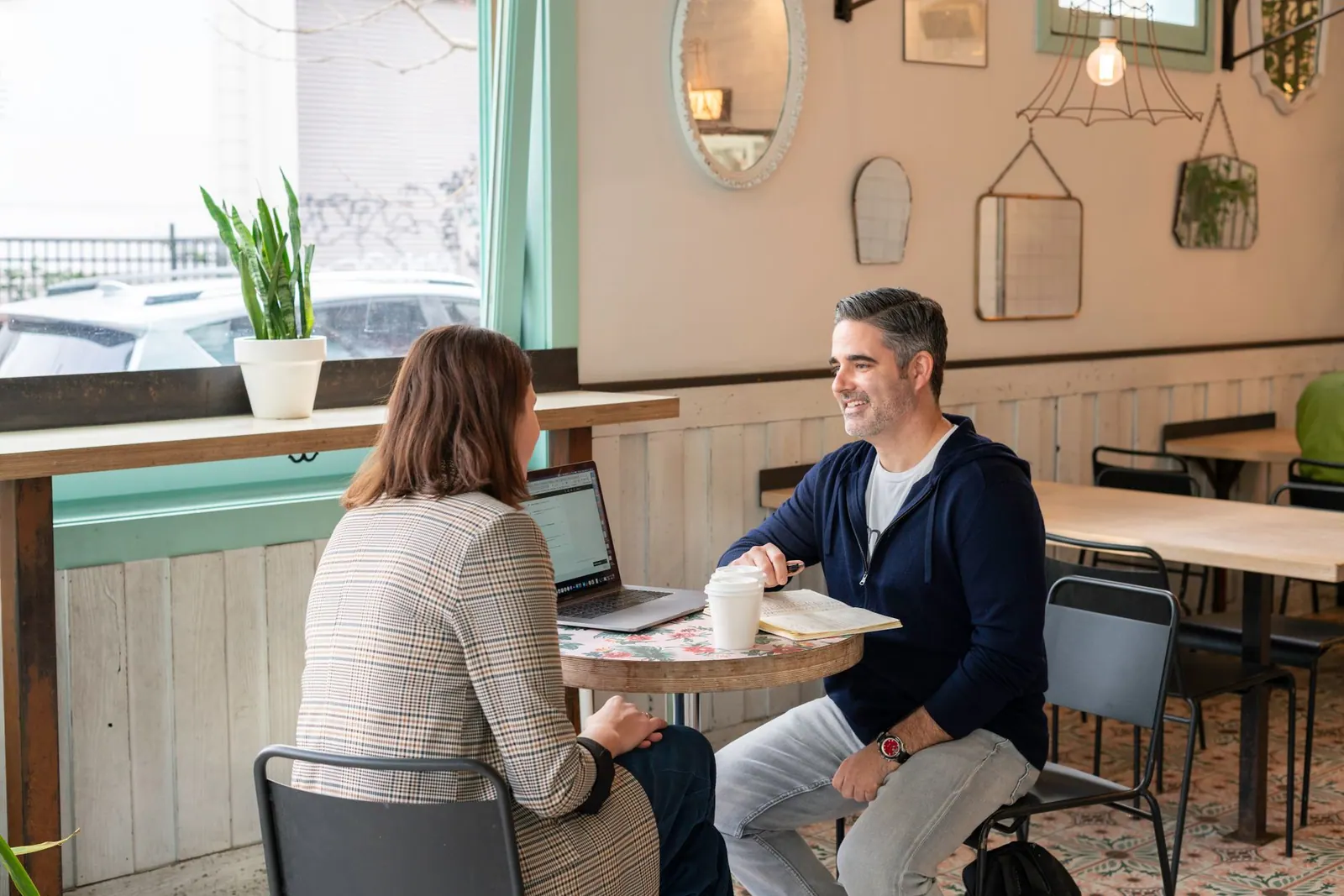 Two adults having a business discussion over coffee in a modern cafe setting.