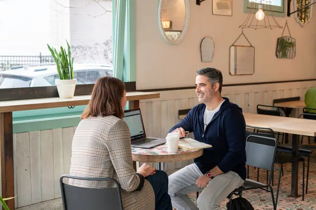 Two adults having a business discussion over coffee in a modern cafe setting.