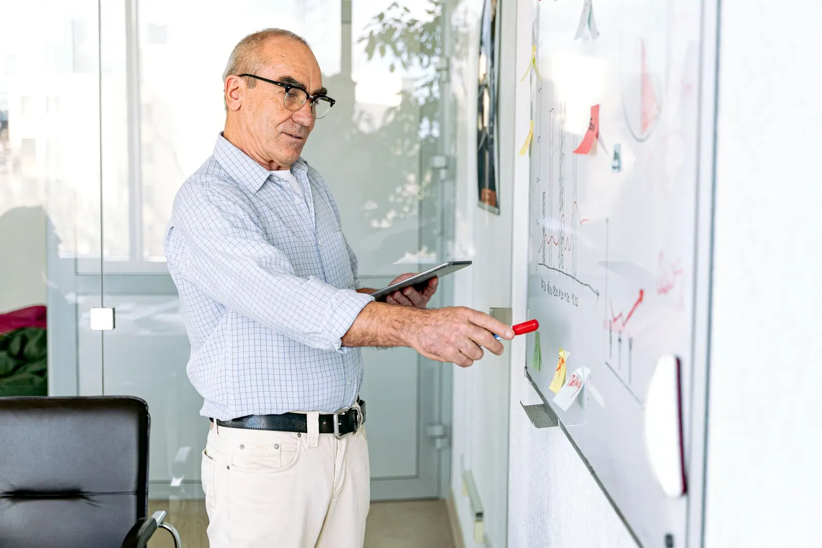 Senior man explaining data on a whiteboard, highlighting teamwork in a modern office.