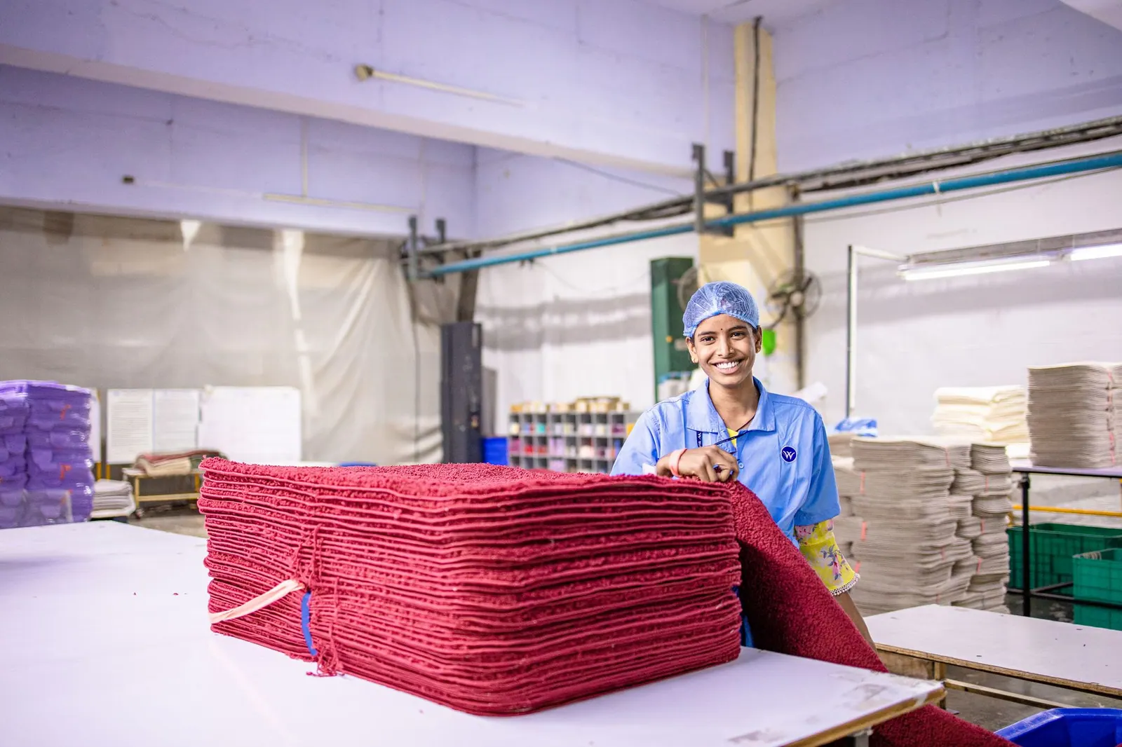 Smiling worker in a textile factory organizing red fabrics on a table.