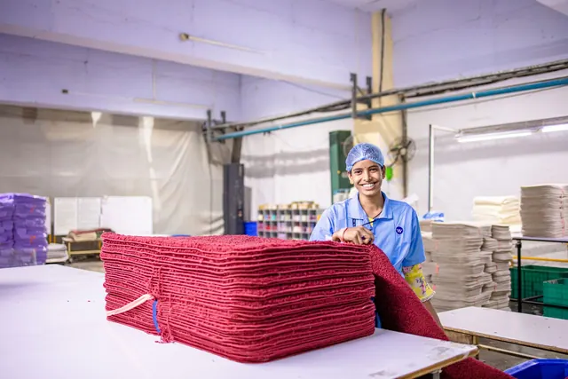 Smiling worker in a textile factory organizing red fabrics on a table.