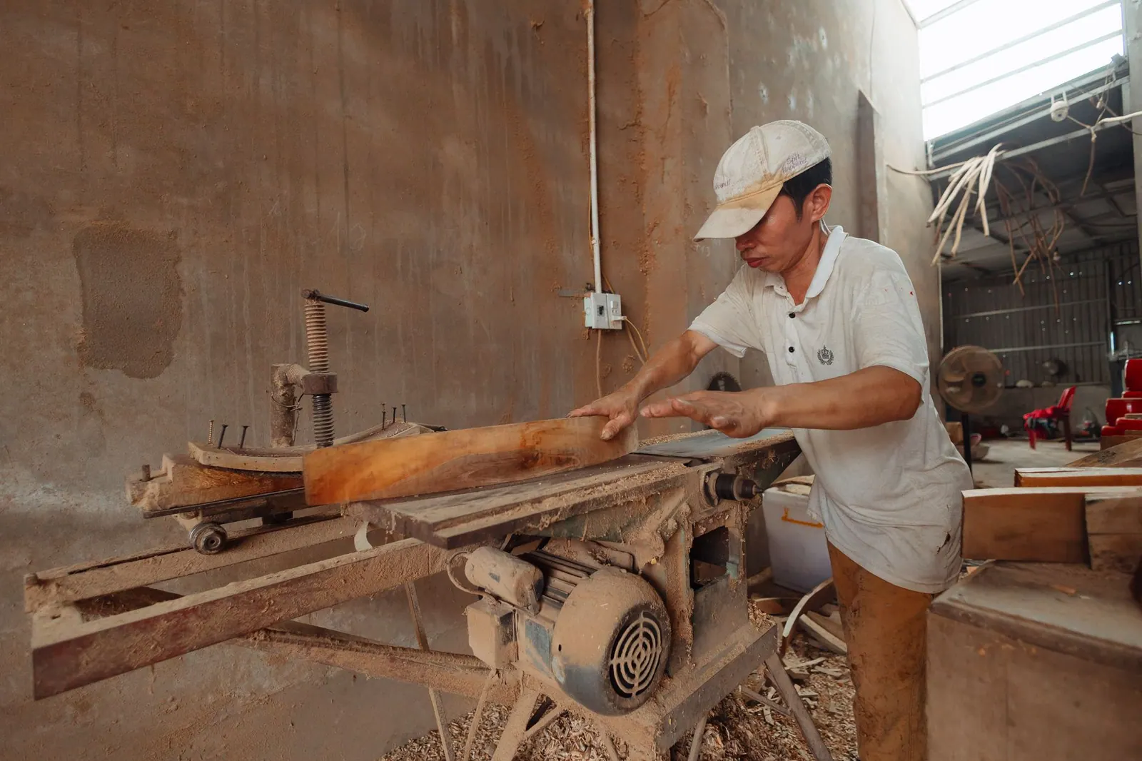A carpenter in a dusty workshop precisely cuts wood using an industrial saw.