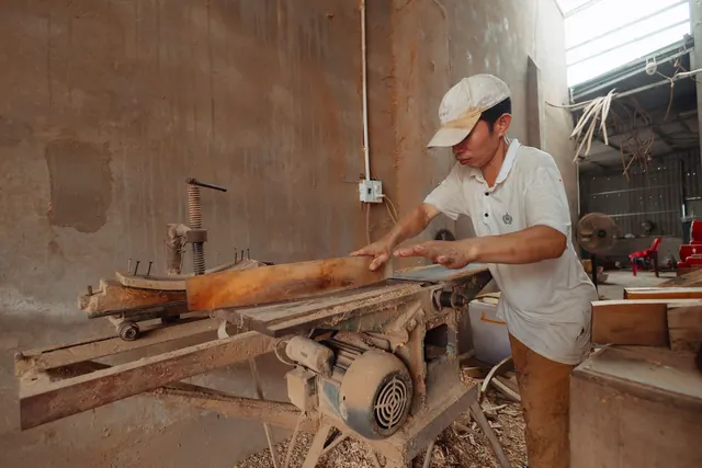 A carpenter in a dusty workshop precisely cuts wood using an industrial saw.