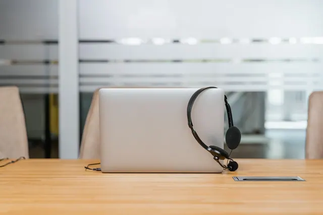 An office setup with a laptop and headset on a wooden table, ideal for remote work.