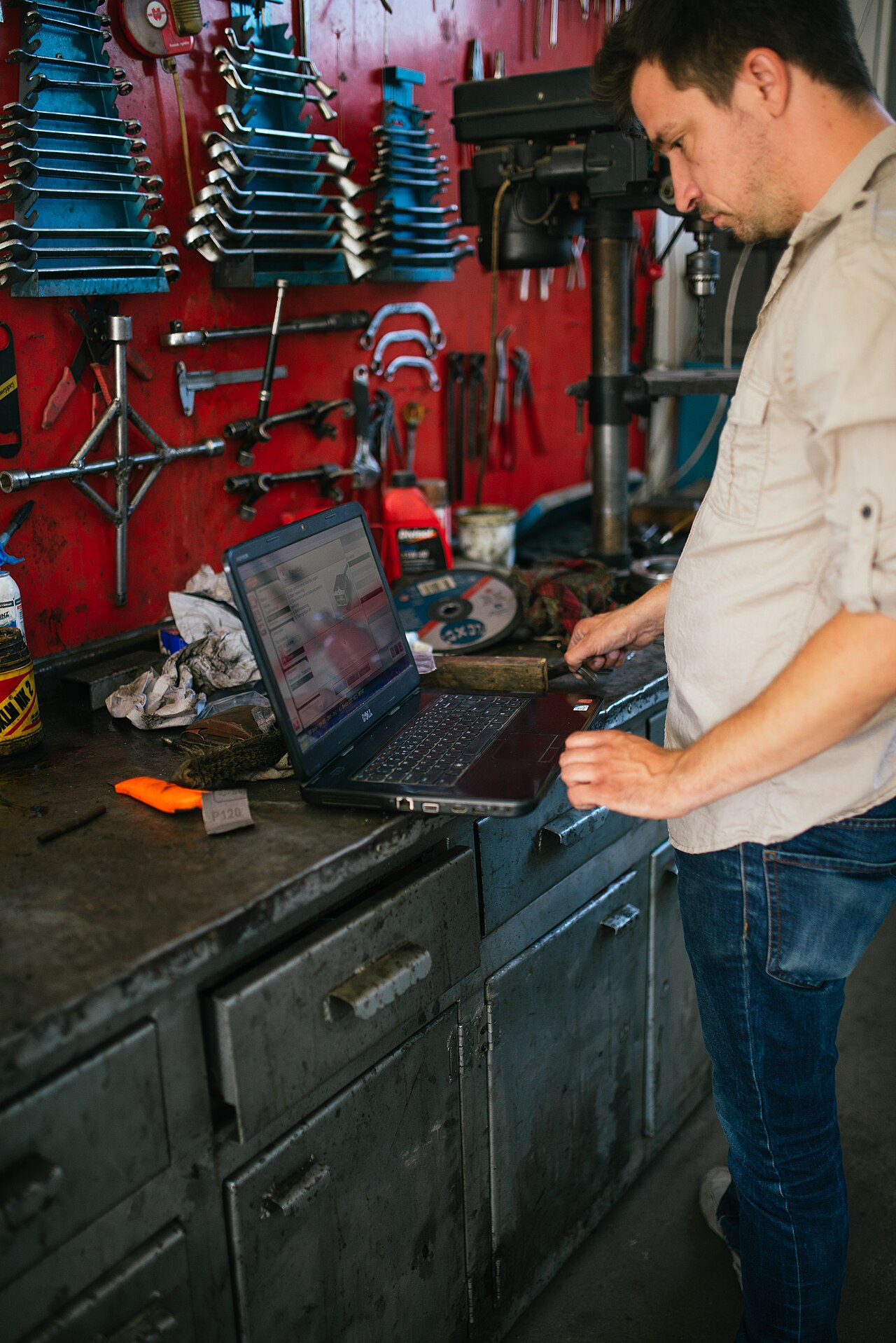 Mann nutzt Laptop in einer Werkstatt mit Werkzeugwand