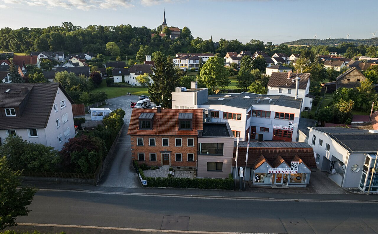 Luftaufnahme eines Dorfes mit Gewerbebetrieb 'HEIDENREICH' und 'RAUMAUSSTATTUNG'
