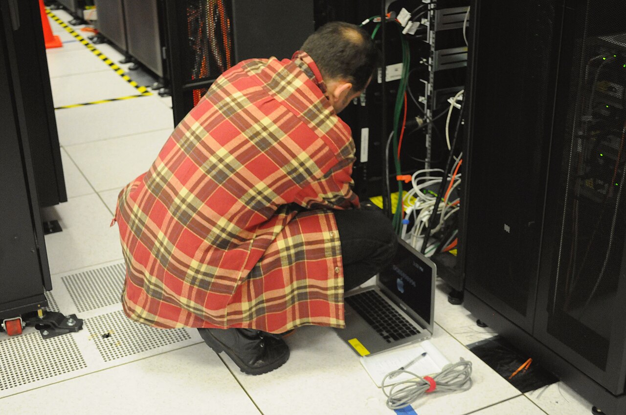 Techniker arbeitet an einem Serverrack mit vielen Kabeln und Laptop