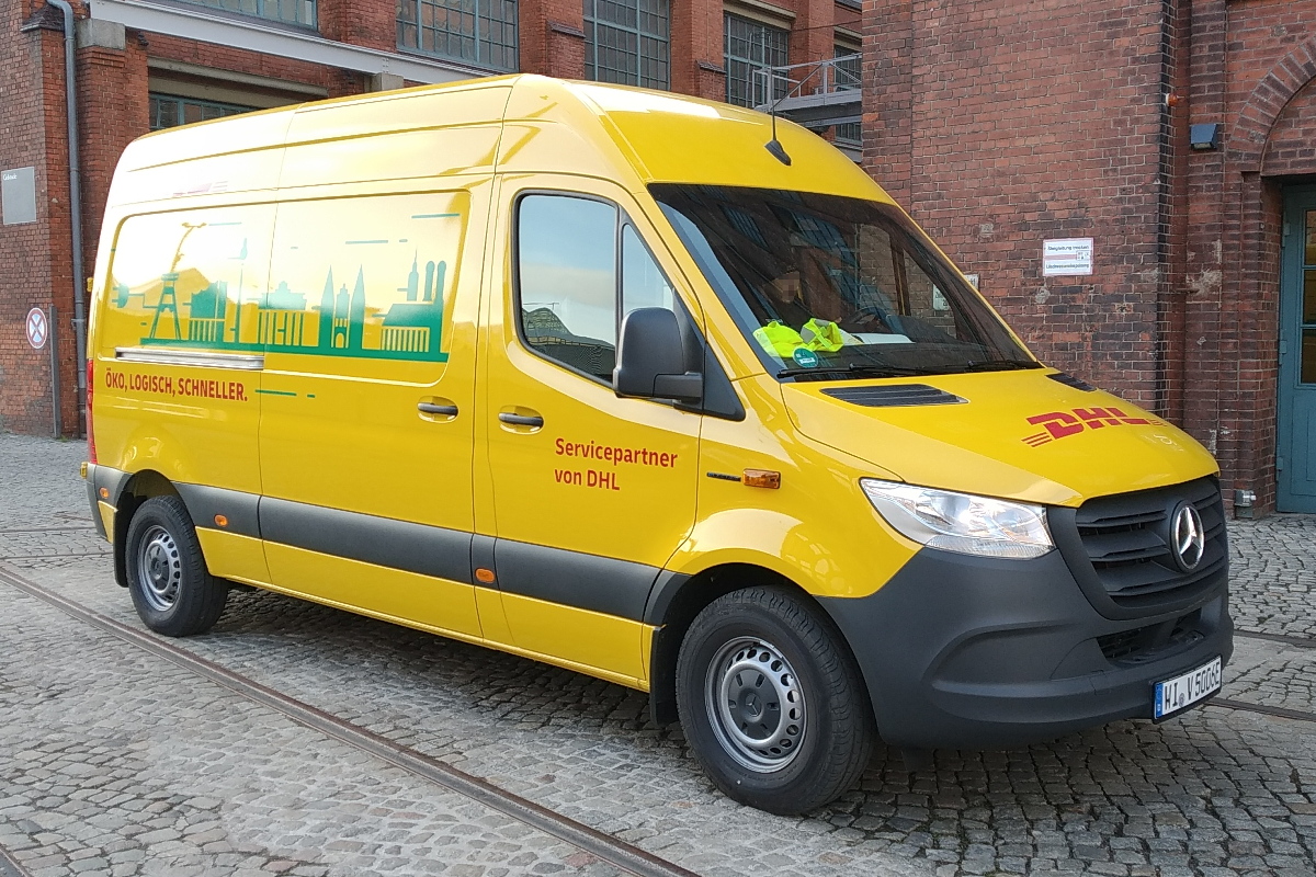 Gelber Lieferwagen mit Skyline-Grafik auf Kopfsteinpflaster vor rotem Backsteingebäude