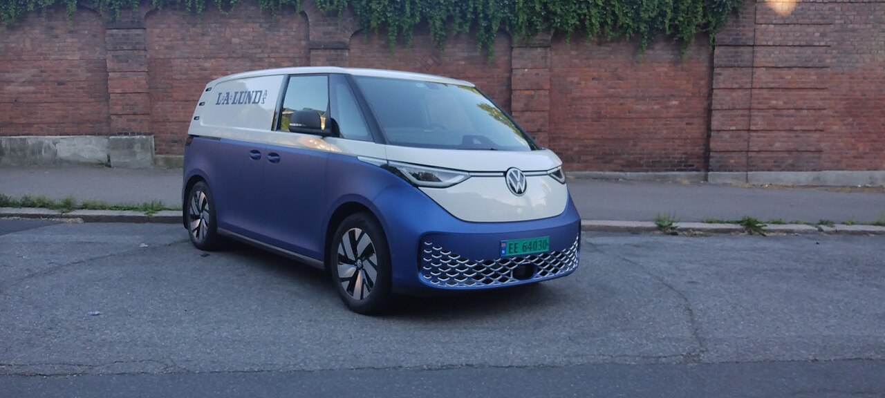 Schrägansicht eines blau-weißen VW ID. Buzz Cargo mit grünem Kennzeichen vor einer efeubewachsenen Ziegelmauer