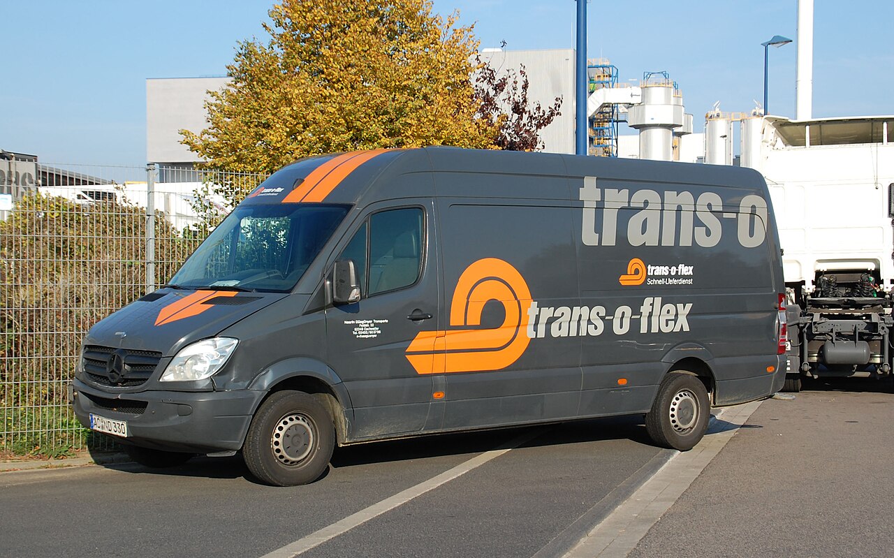 Dunkelgrauer Lieferwagen mit trans-o-flex Beschriftung auf einer Straße