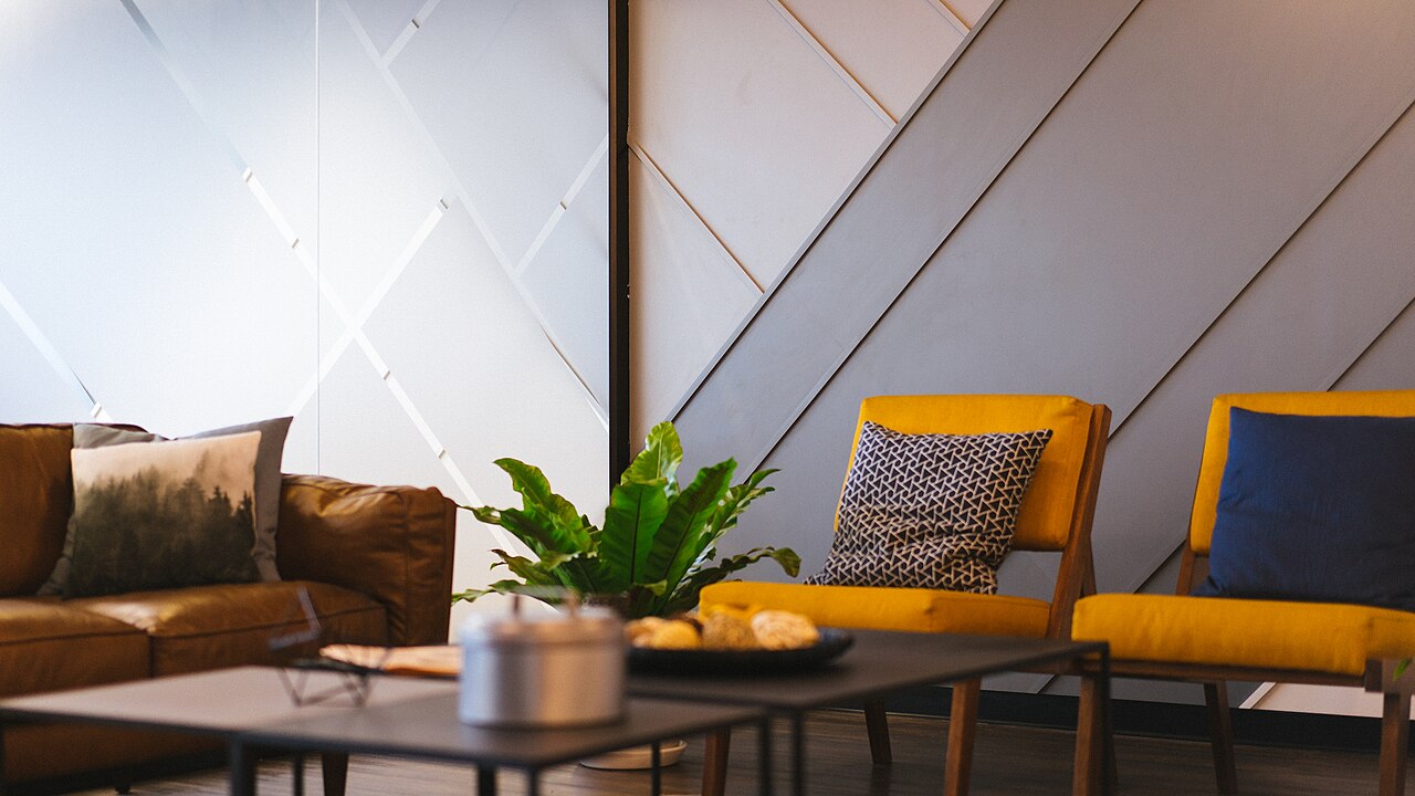 Besprechungsecke mit braunem Sofa, gelben Sesseln und Topfpflanze in einem Coworking-Bereich