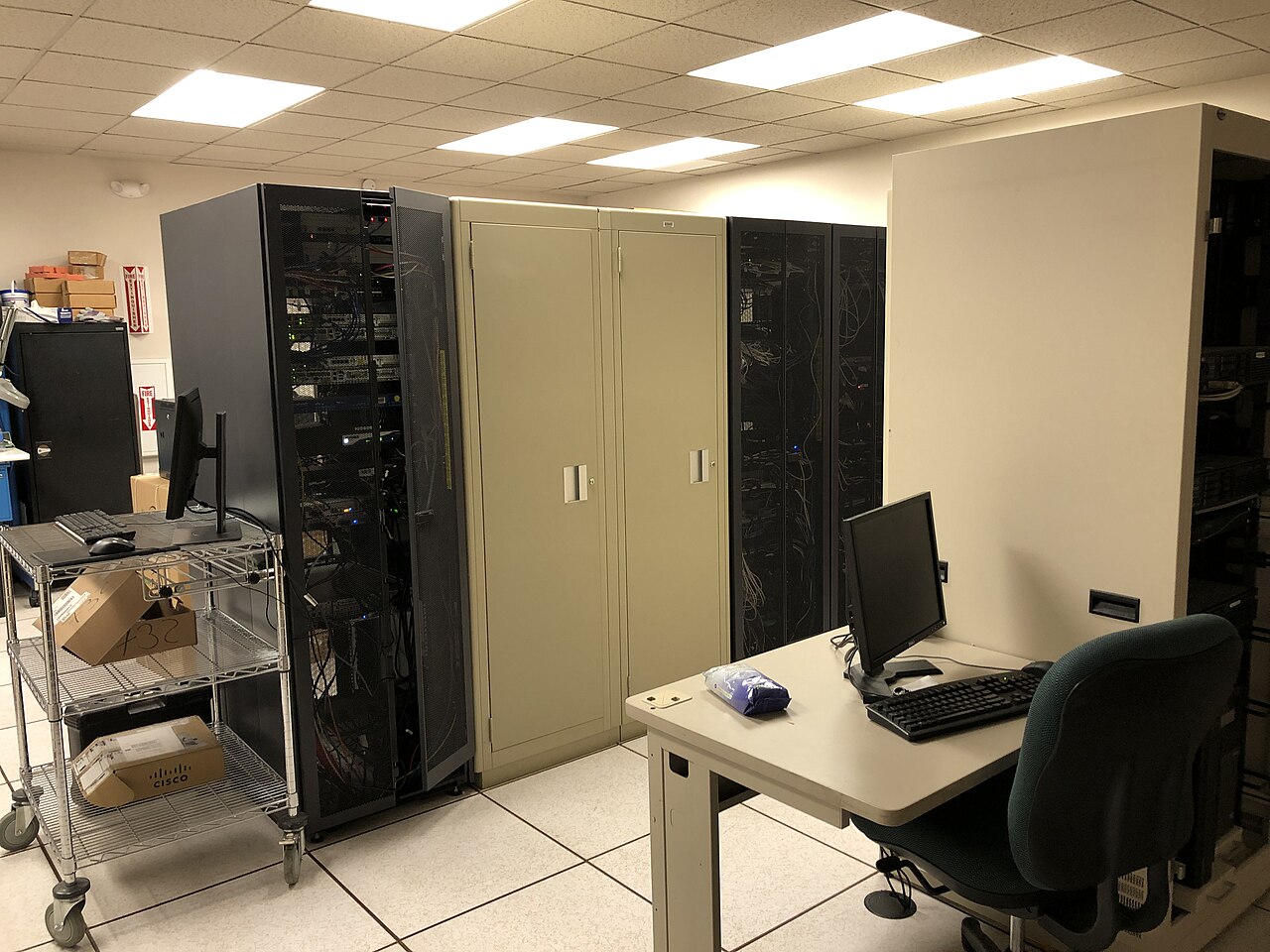 Serverraum mit Serverschränken, Metallwagen und Schreibtisch mit Computer
