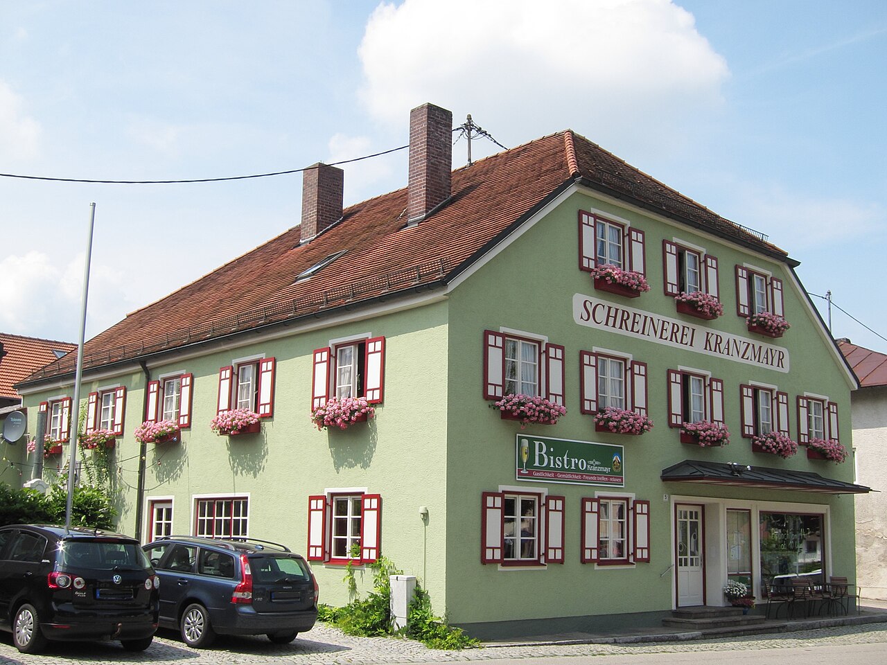 Schreinerei Kranzmayr in Sankt Wolfgang, grün verputztes Gebäude mit Schildern und geparkten Autos